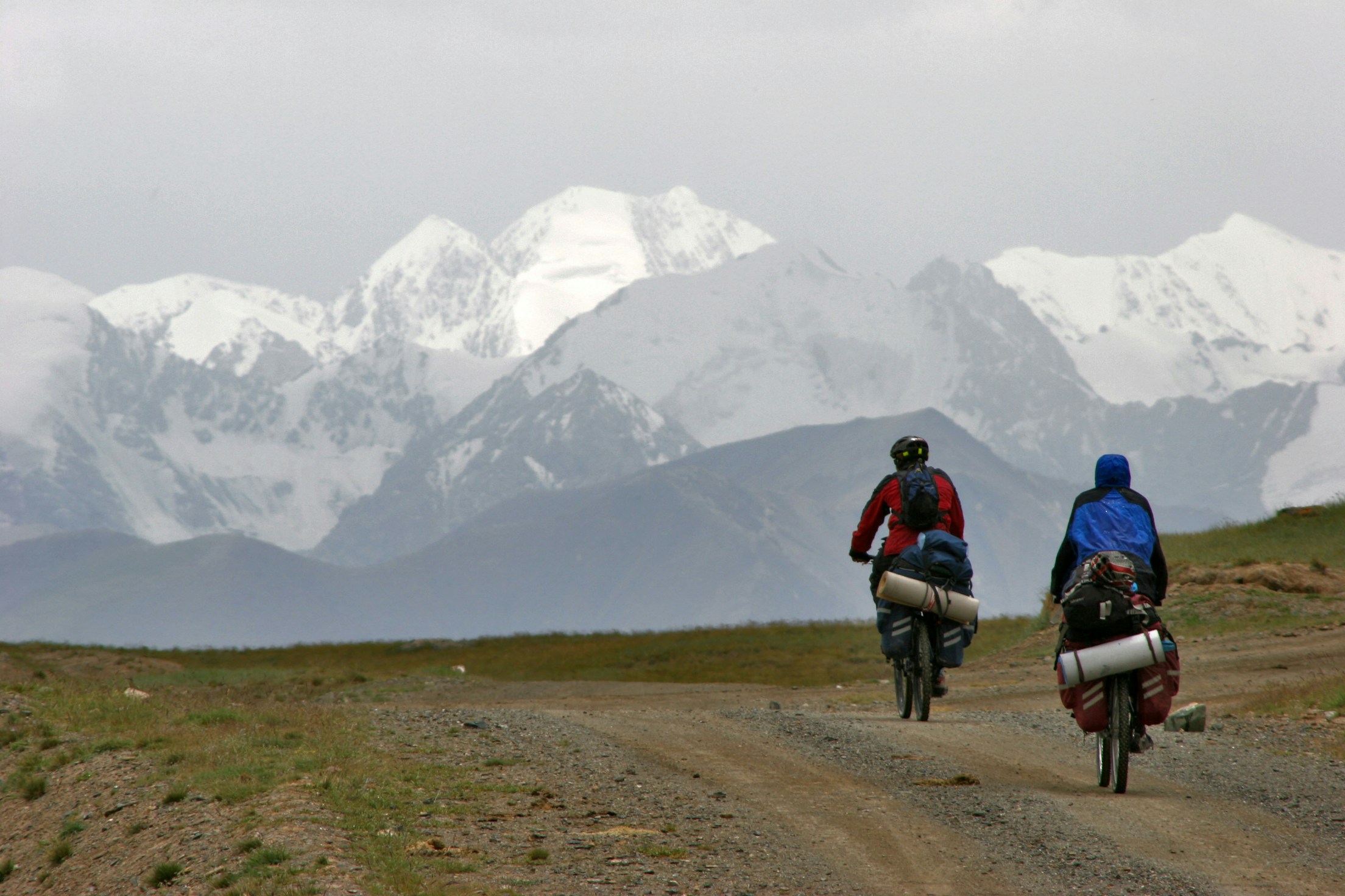 Two loaded touring cyclists riding towards snow-covered mountains; expedition inspiration